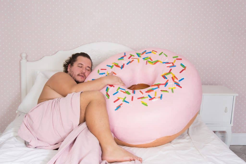 How To Safely Lose Weight Fast Part III: Managing Behavior Man in bed asleep holding a giant donut.