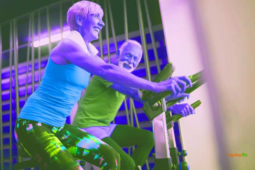 Two older adults laughing while working out on their exercise bikes