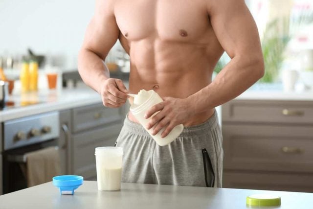 Muscular man scooping protein powder into a shaker bottle
